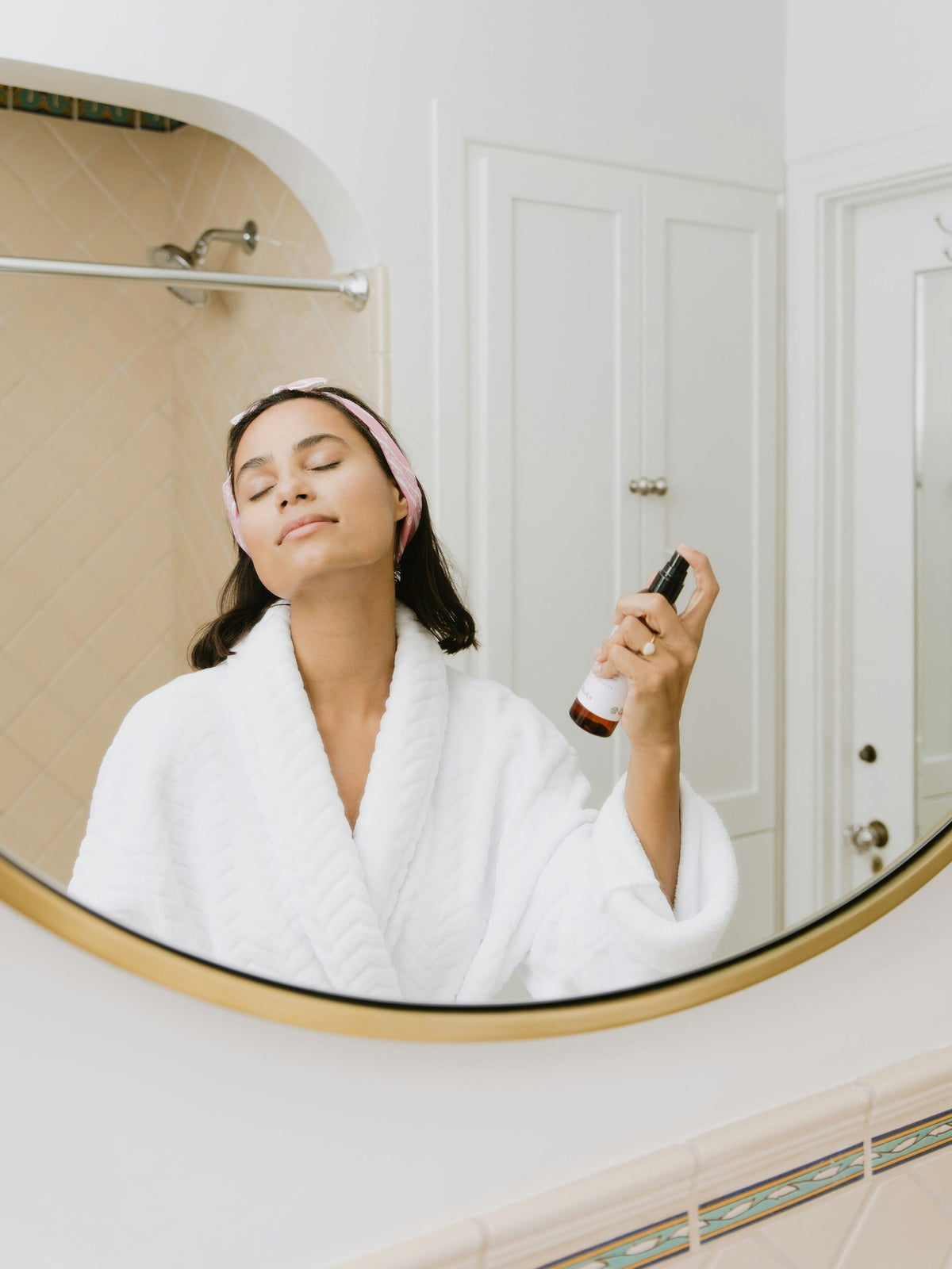 Femme en peignoir blanc prenant soin de sa peau dans une salle de bain lumineuse